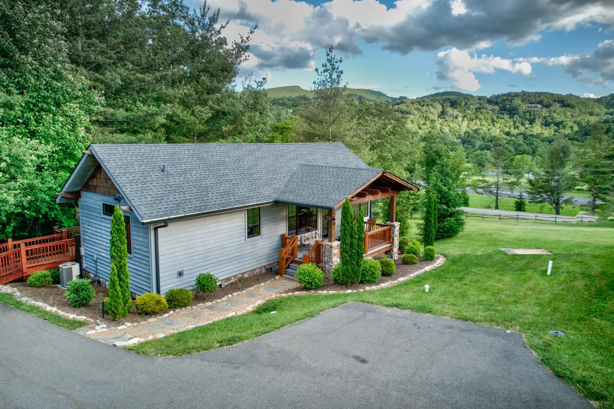 This exterior image highlights a peaceful front porch overlooking a landscaped garden and driveway, with the mountains visible in the background. The porch is set up for relaxation and enjoying the outdoors, offering mountain views and a tranquil ambiance.