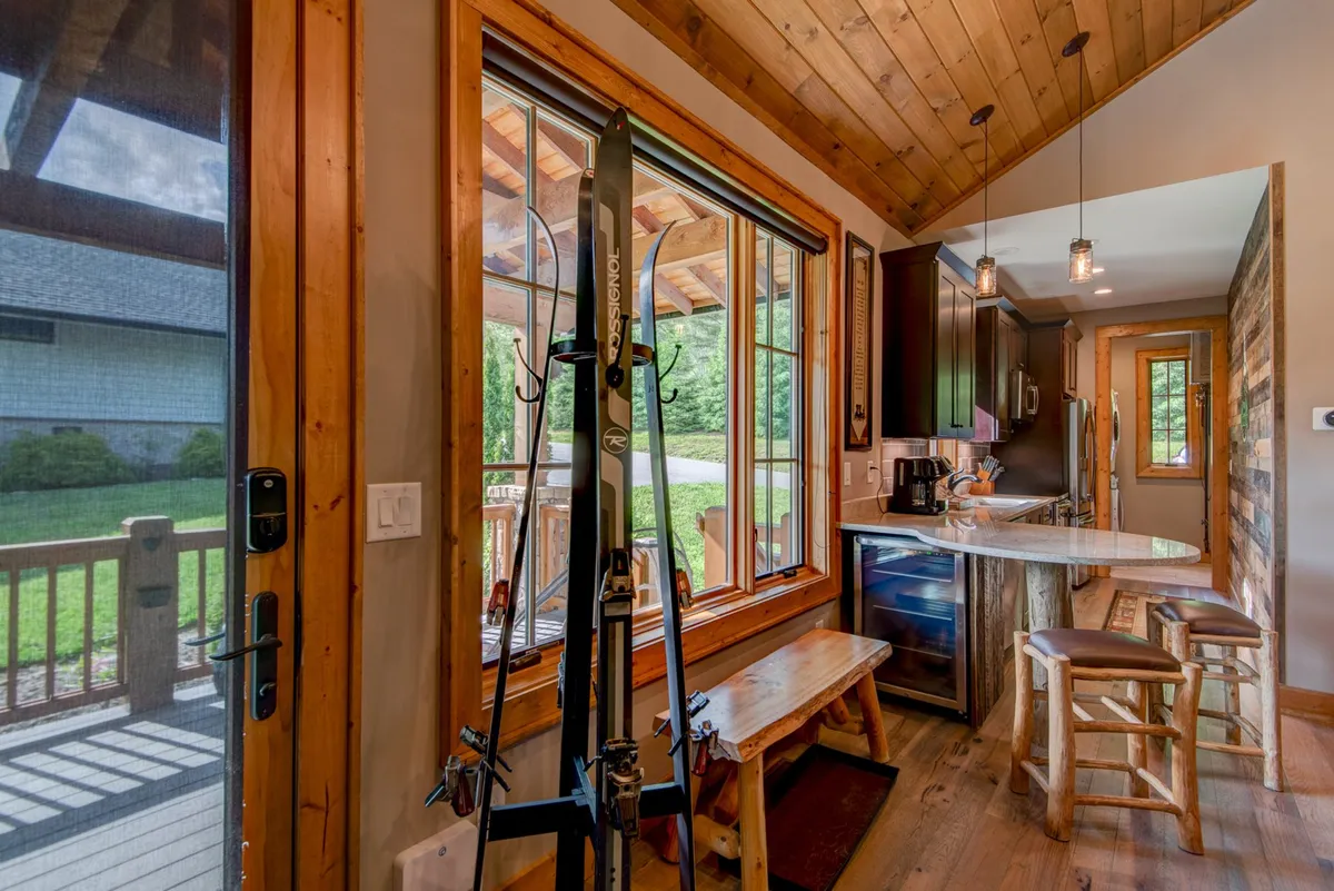 An interior scene featuring ski equipment ready by large windows, wooden countertops, and bar stools. The space is bright and cozy, inviting families to gather, socialize, and prepare for outdoor adventures, with views framing the outside world.