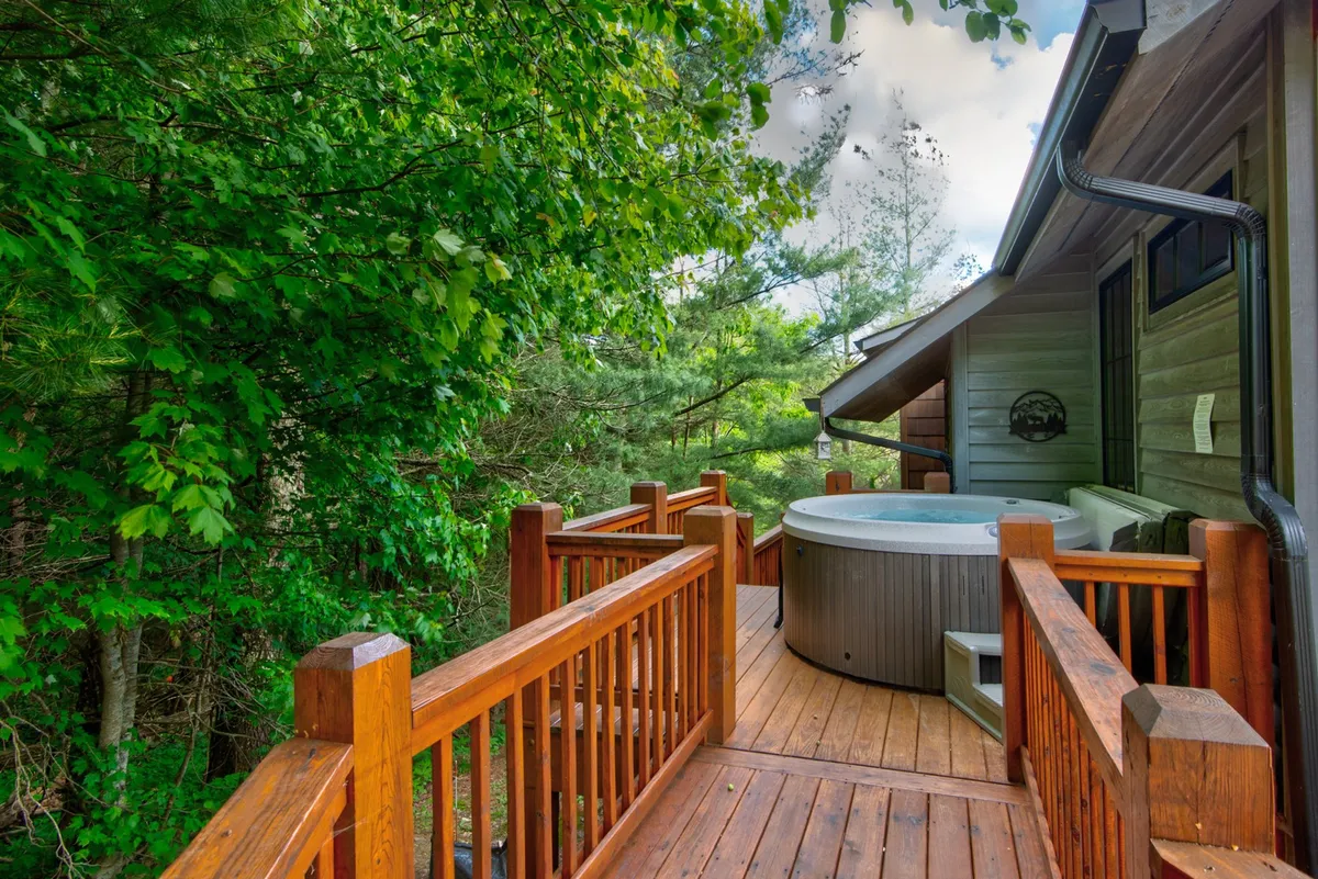 A serene exterior shot showcasing a wooden deck with a hot tub surrounded by lush greenery. The setting suggests relaxation in nature, with space to unwind and appreciate mountain views or stargaze after a day of outdoor adventure.