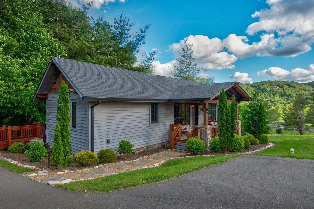 The image depicts a charming single-family mountain cabin set amidst lush landscaping and mature trees. The spacious porch, adorned with comfortable seating, overlooks a beautifully manicured garden, inviting guests to relax and take in the surrounding natural beauty. The cabin exudes warmth and tranquility, offering both privacy and a sense of connection to the outdoors.