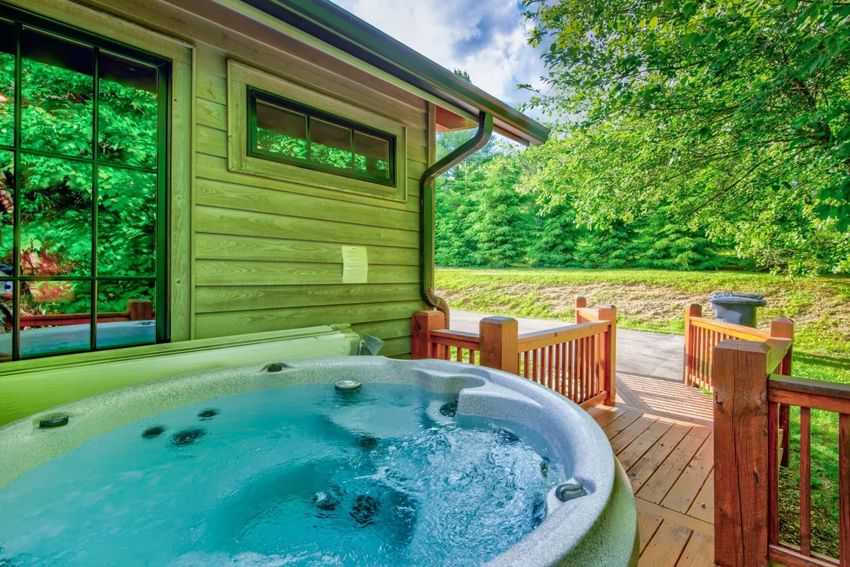 Another angle on the deck, focusing on the hot tub and multiple seating options. The wooden deck is bordered by lush greenery, inviting guests to enjoy coffee in the morning or conversation in the evening. The image emphasizes the multi-tiered layout of the deck.