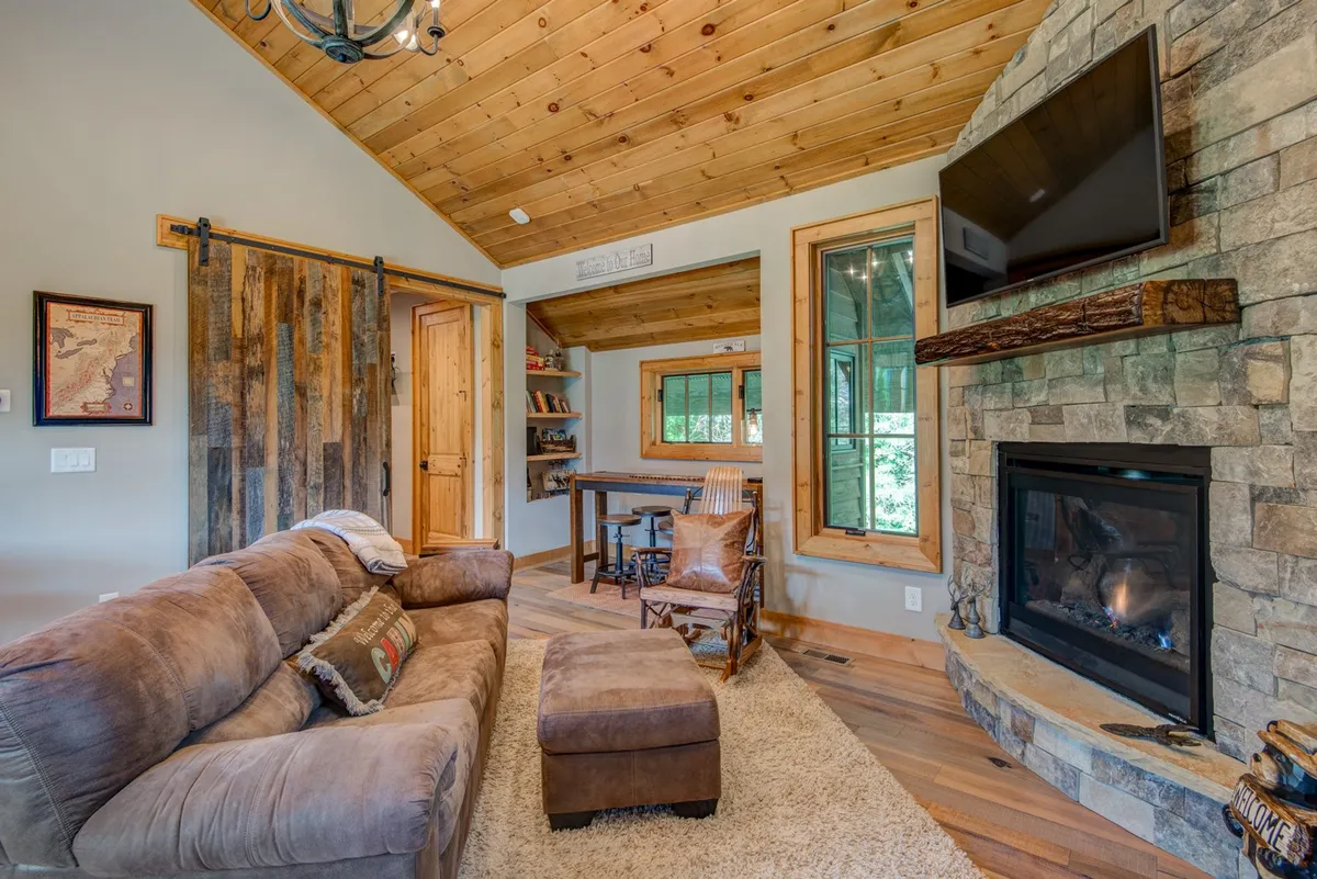 A cozy living room featuring a comfortable sofa, a warm fireplace with wooden beams overhead, and large windows that let in natural light and offer views of the Elk River Valley. The space is tastefully decorated with inviting touches, making it ideal for relaxation and togetherness.