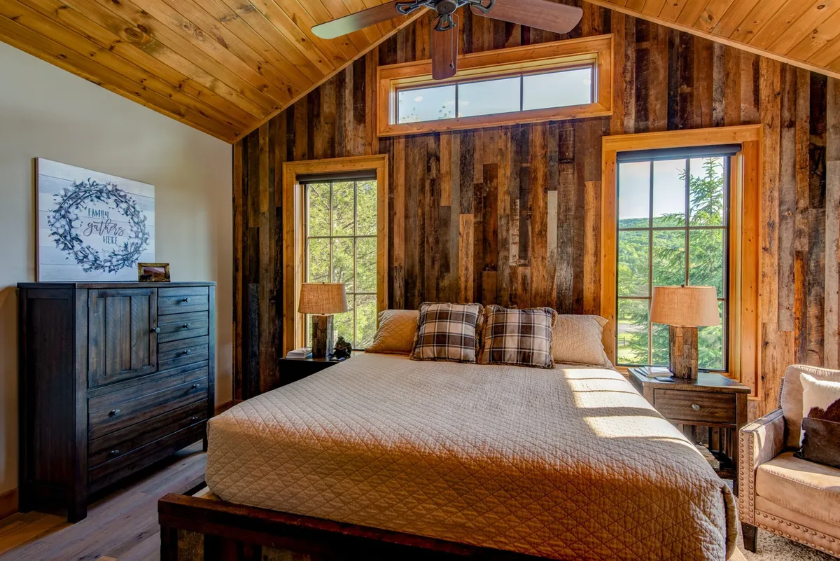 A tranquil bedroom showcasing a well-made bed with decorative pillows, a wooden dresser, dual bedside lamps, and expansive windows that let in morning sunlight. The space exudes serenity and modern comfort, perfect for restful nights.