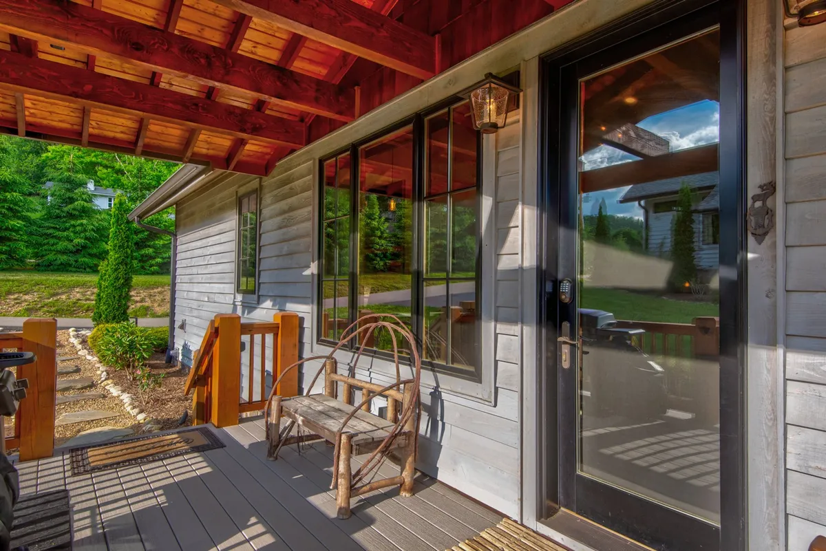 A welcoming front porch featuring a wooden rocking chair, exposed beams, and a landscaped yard. The scene evokes tranquility and a classic mountain retreat experience, ideal for savoring the views and mountain air in any season.