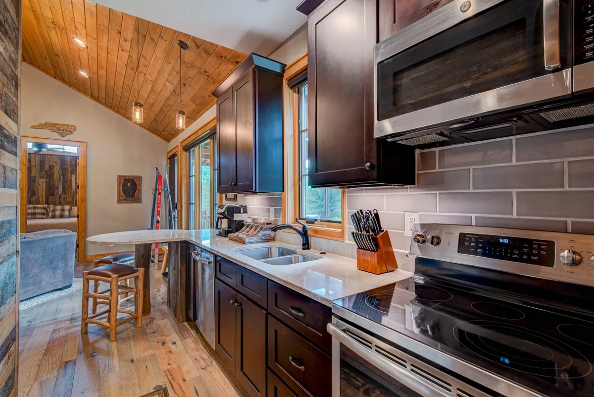 A stylish kitchen with modern GE appliances, dark cabinetry, marble countertops, and wooden bar stools. The kitchen's layout is ideal for cooking, entertaining, and casual dining, with a welcoming and functional feel.