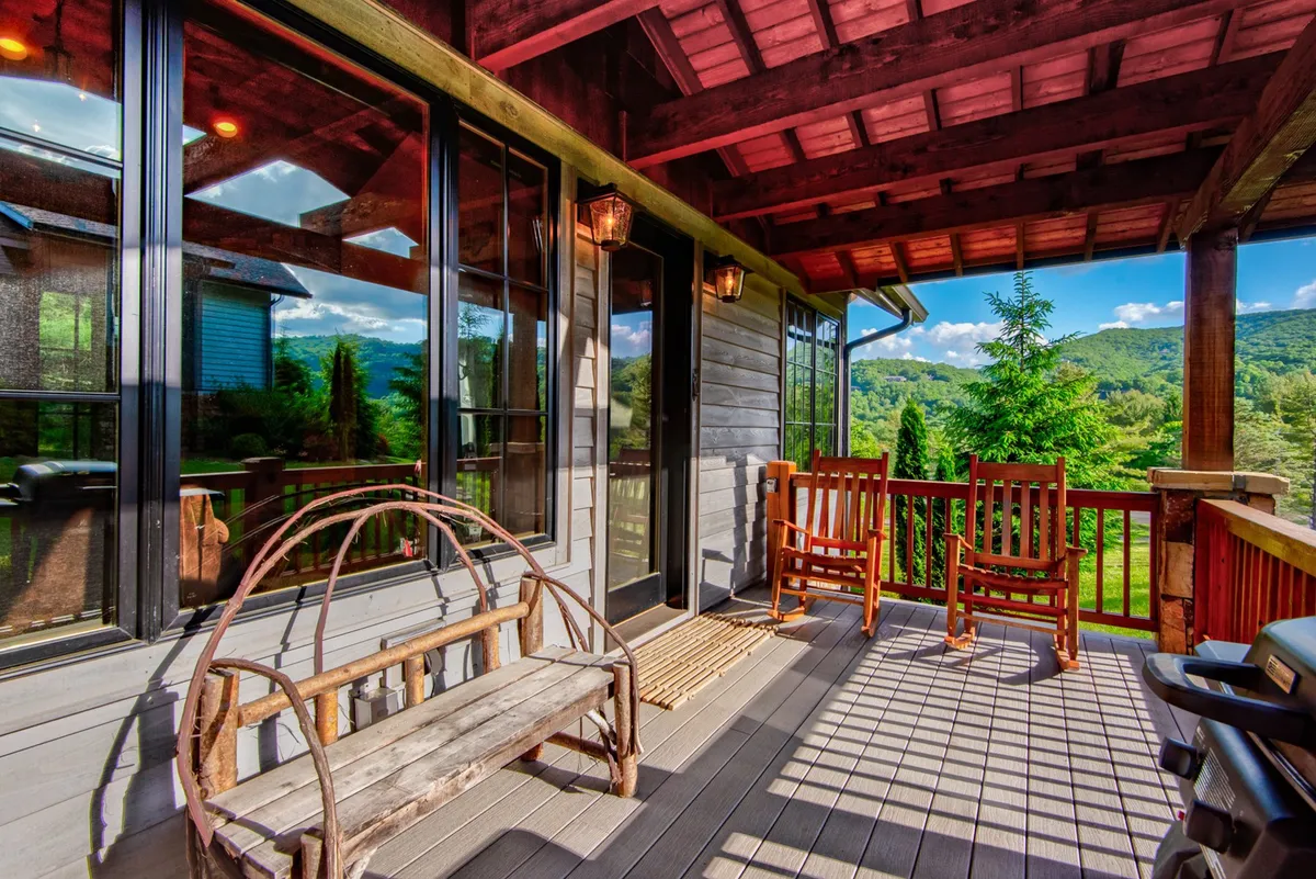 The exterior shot highlights wooden rocking chairs and a rustic bench on a porch, overlooking a peaceful green landscape. Large glass doors connect indoor and outdoor living, while the tranquil setting suggests spaces for evening conversations or morning coffee with a view.